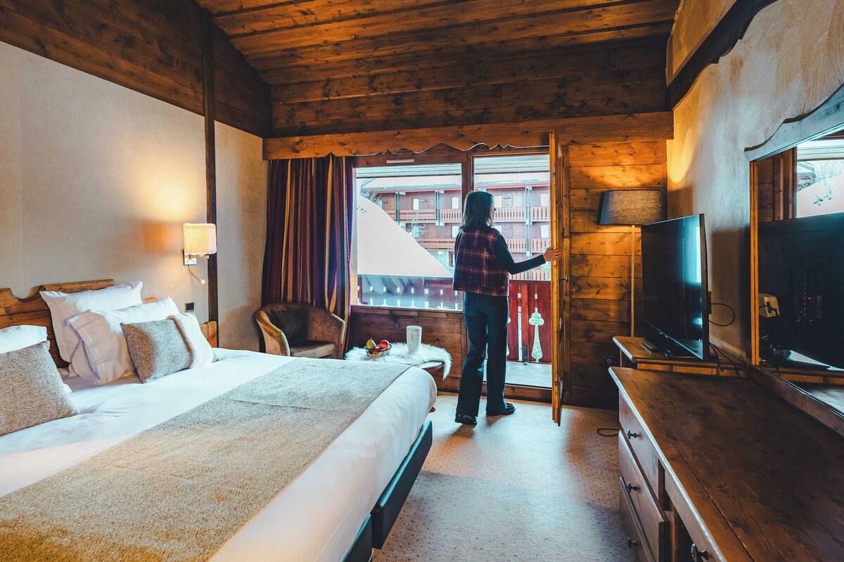 A hotel room with a bed, a chair, a TV, and a balcony with curtains.