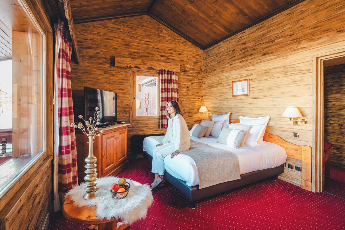A wooden cabin room with a bed, a television, and a fruit basket on a side table.