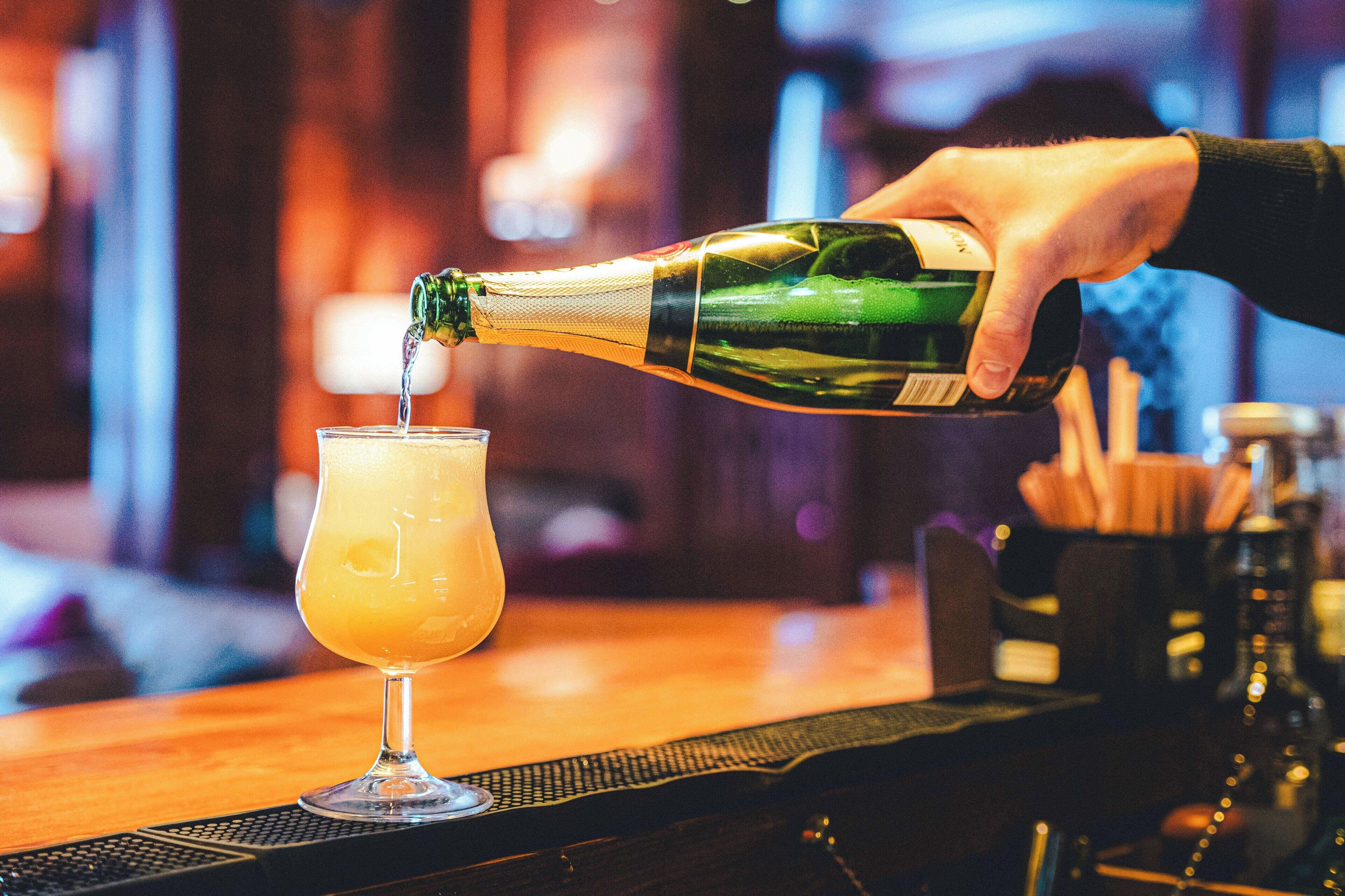 A hand pouring a drink from a green bottle into a glass.