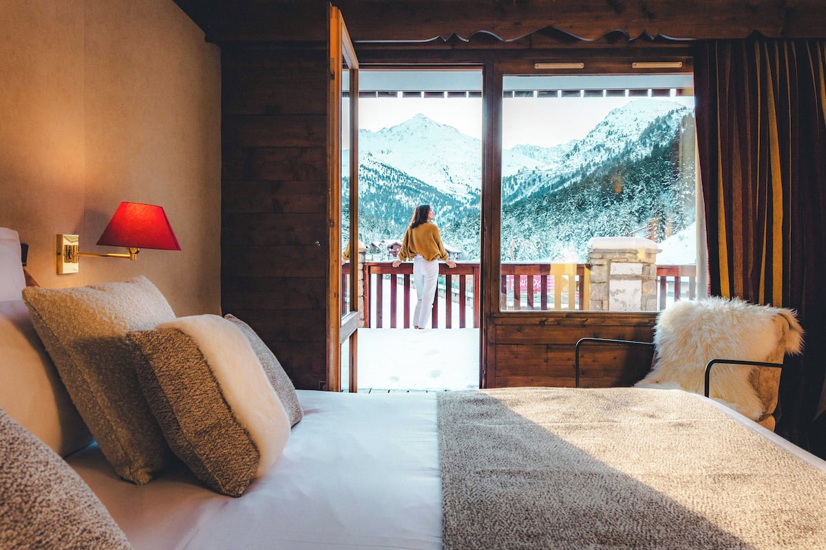 A bedroom with a bed, a red lamp, and a view of snow-covered mountains through an open door.
