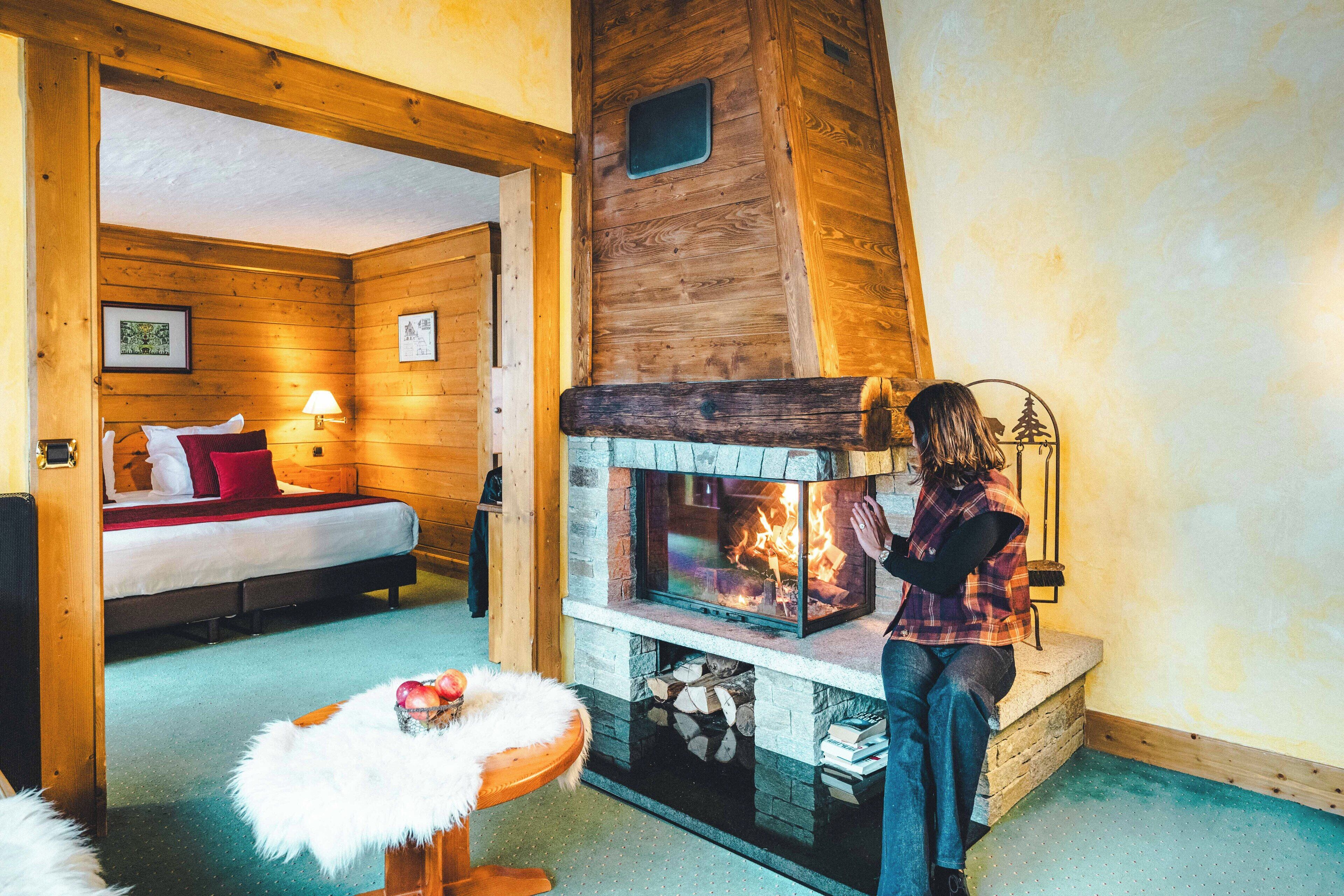 L’intérieur d’un chalet confortable en bois, avec une cheminée, un lit agrémenté d’oreillers rouges et un fauteuil moelleux blanc.