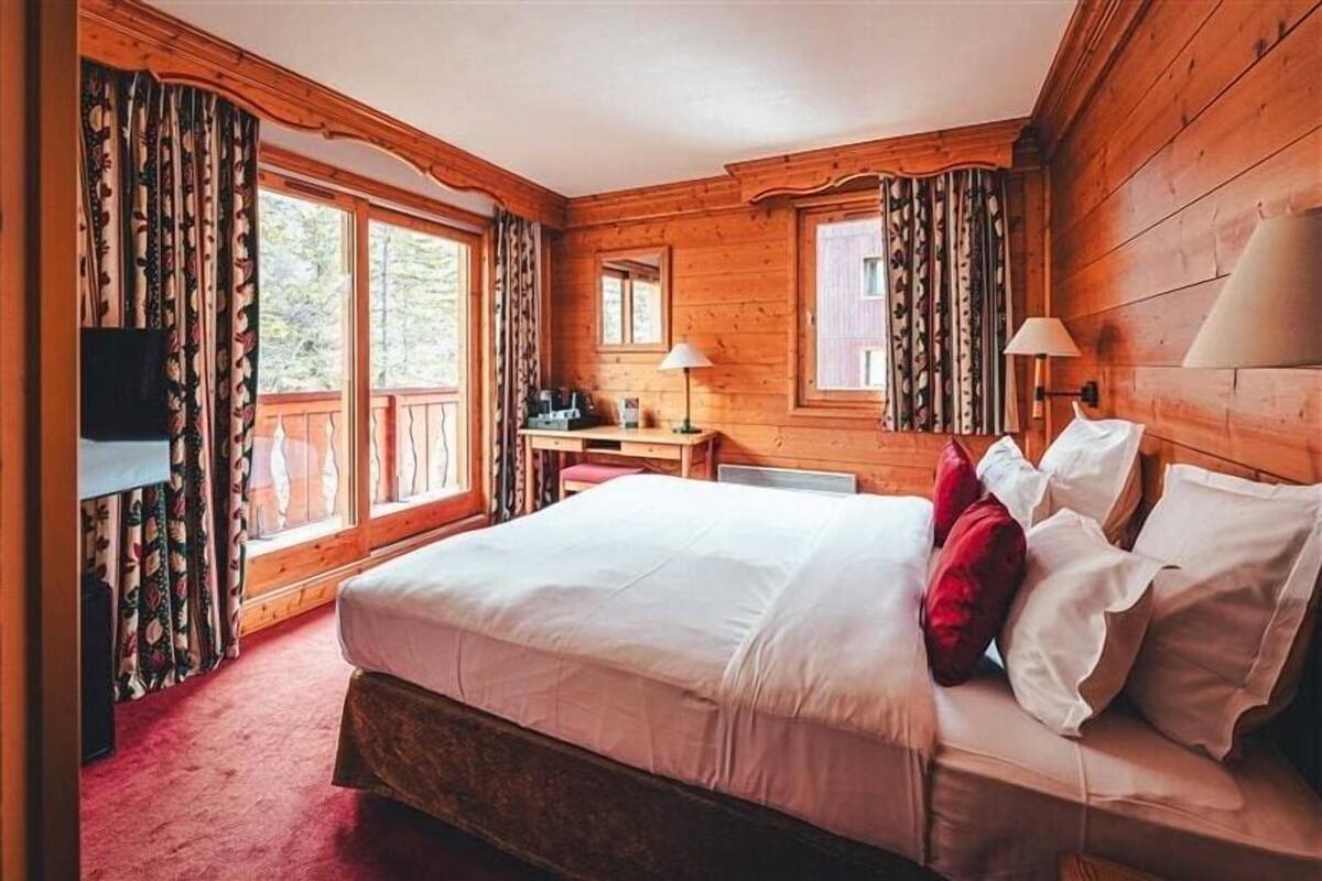 A wooden cabin room with a bed, a desk, and a TV.