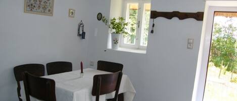 Un comedor con una mesa preparada para cuatro, una ventana con vistas y una puerta que da al exterior.
