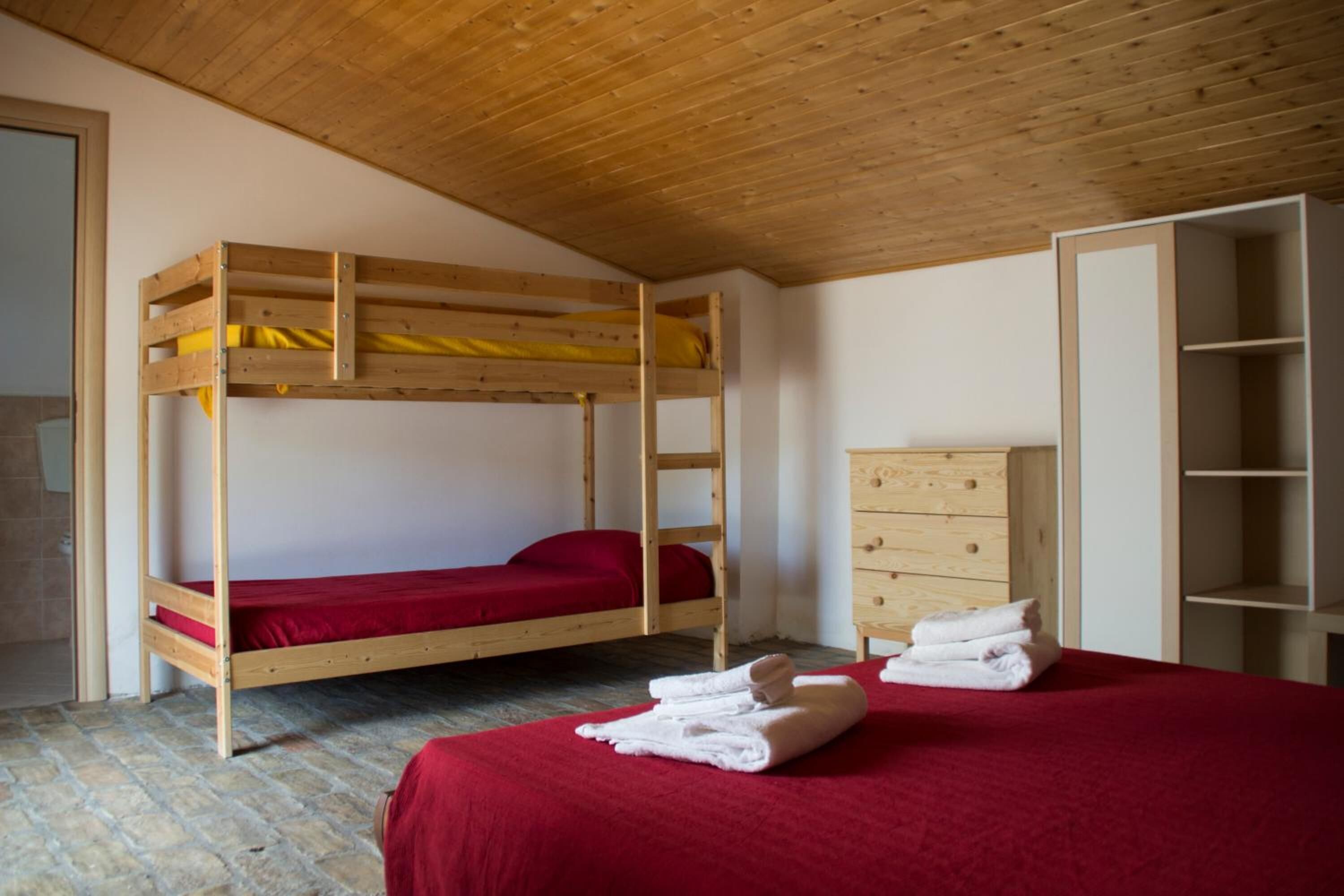 Habitación con literas, techo de madera, colcha roja y cómoda de madera.