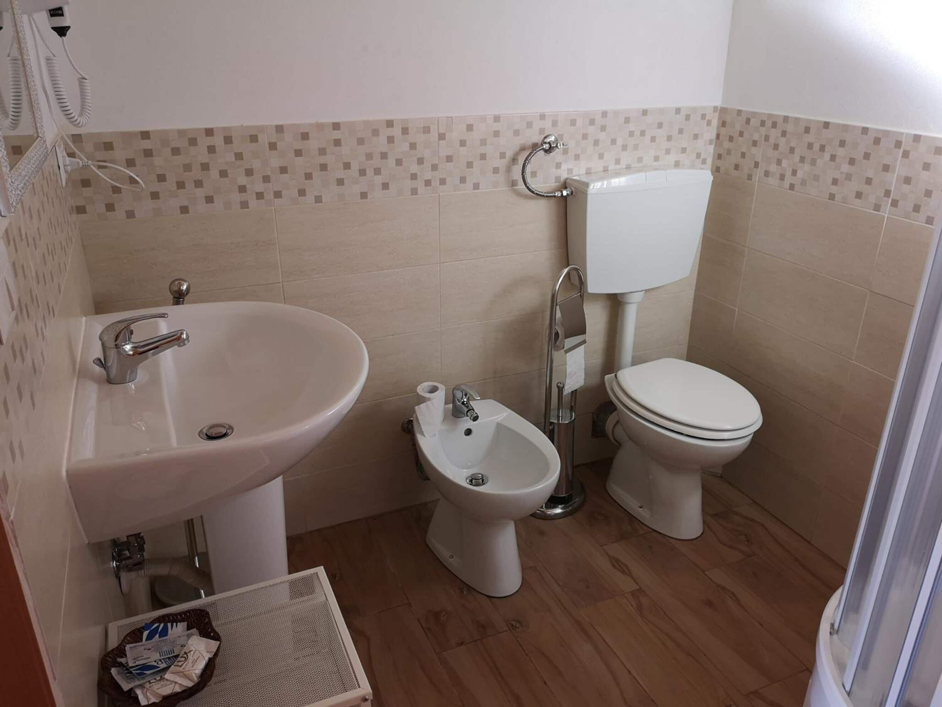 A bathroom with a sink, bidet, toilet, and a small basket of toiletries.