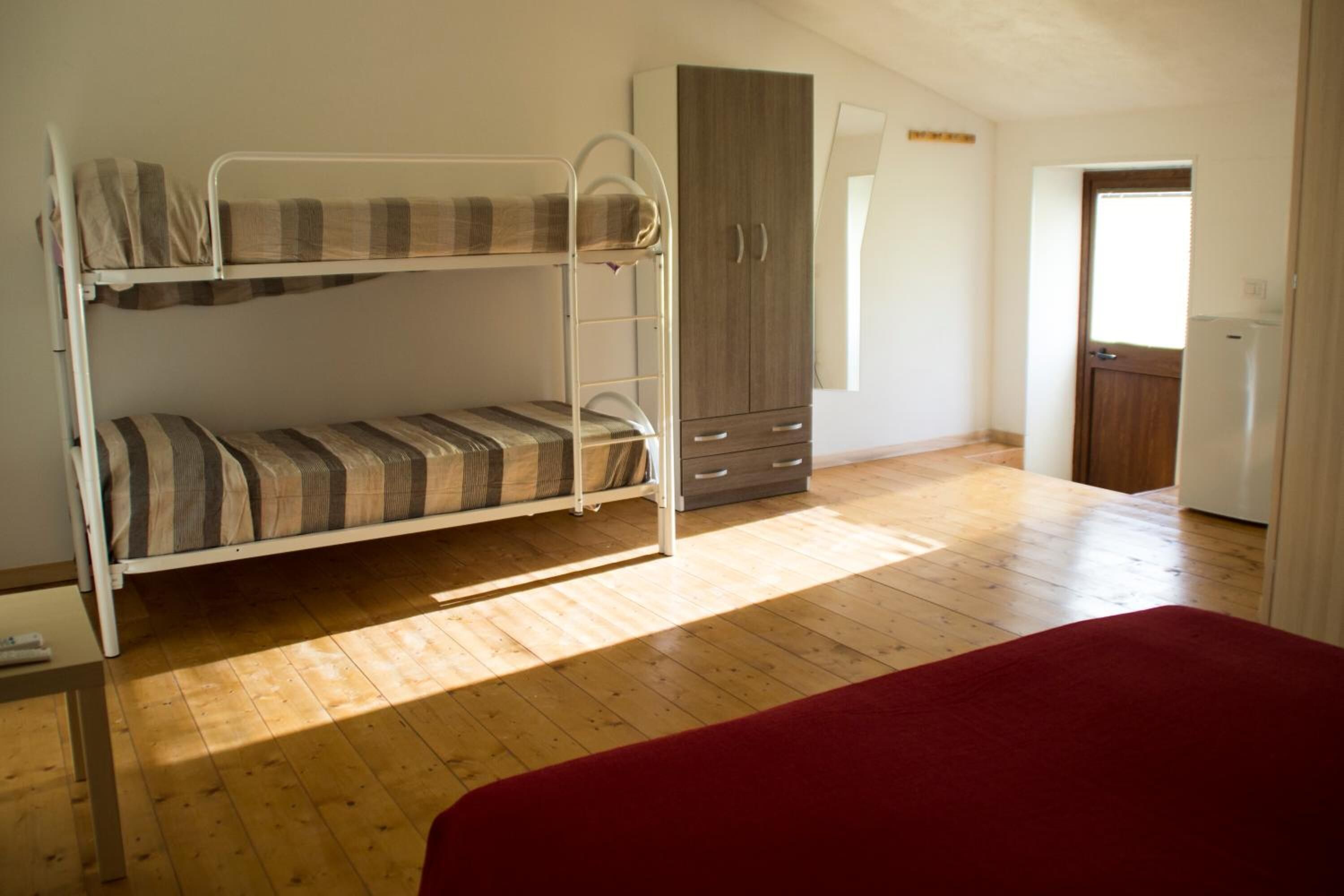 A room with a bunk bed, a wardrobe, and a door leading to another room.