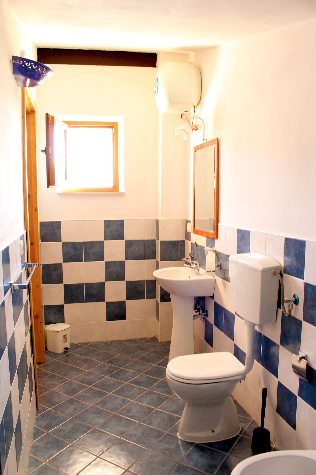 A small bathroom with a white toilet, a sink, and a mirror. The walls are tiled in a blue and white checkered pattern.