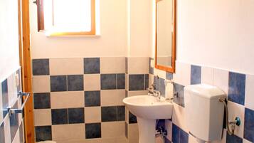 A small bathroom with a white toilet, a sink, and a mirror. The walls are tiled in a blue and white checkered pattern.