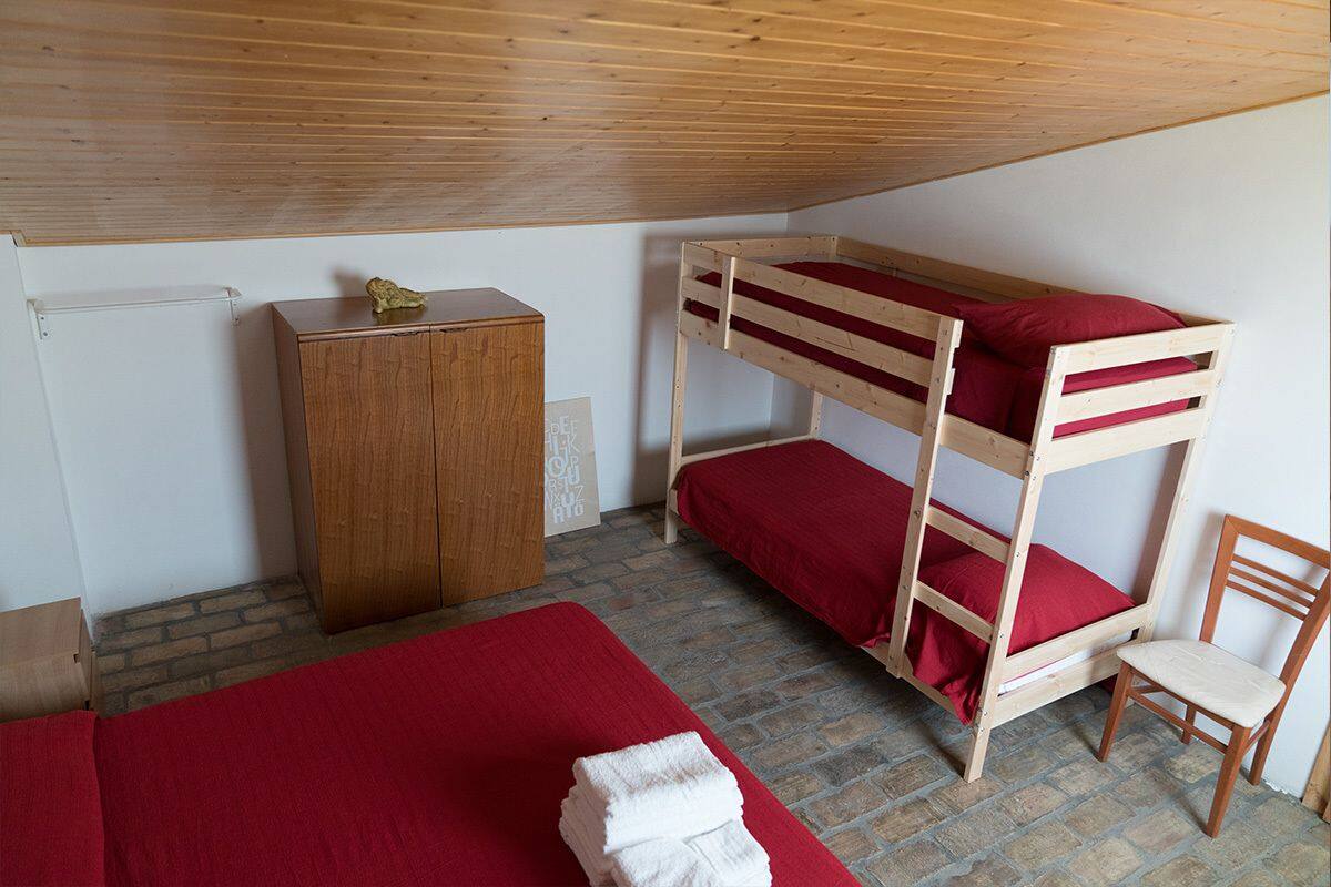 Een stapelbed met rode beddengoed, een houten garderobe, een stoel en een rode deken op de vloer.