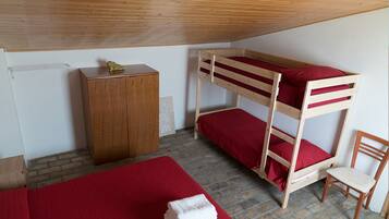 A bunk bed with red bedding, a wooden wardrobe, a chair, and a red blanket on the floor.