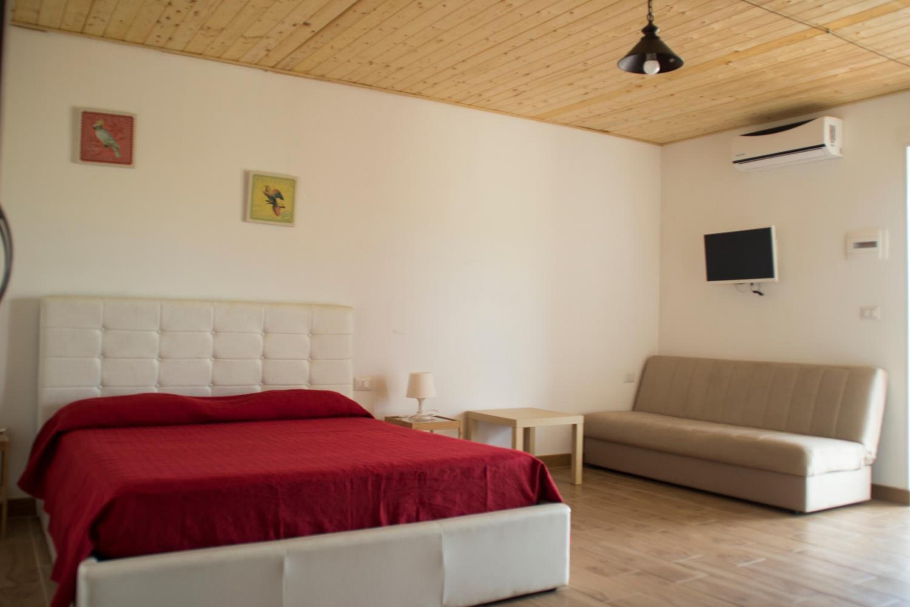 Ein Schlafzimmer mit einem weißen Bett, einem beigen Sofa und zwei an der Wand befestigten Fernsehgeräten.