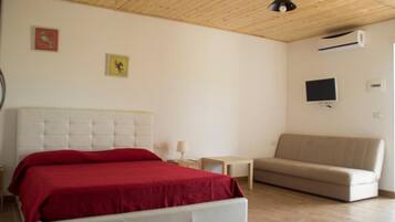 Ein Schlafzimmer mit einem weißen Bett, einem beigen Sofa und zwei an der Wand befestigten Fernsehgeräten.