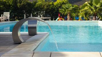 A swimming pool with a modern water feature, surrounded by palm trees and lounge chairs.