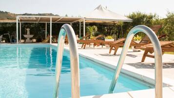 A swimming pool with metal ladders, lounge chairs, and a covered area with a white canopy.