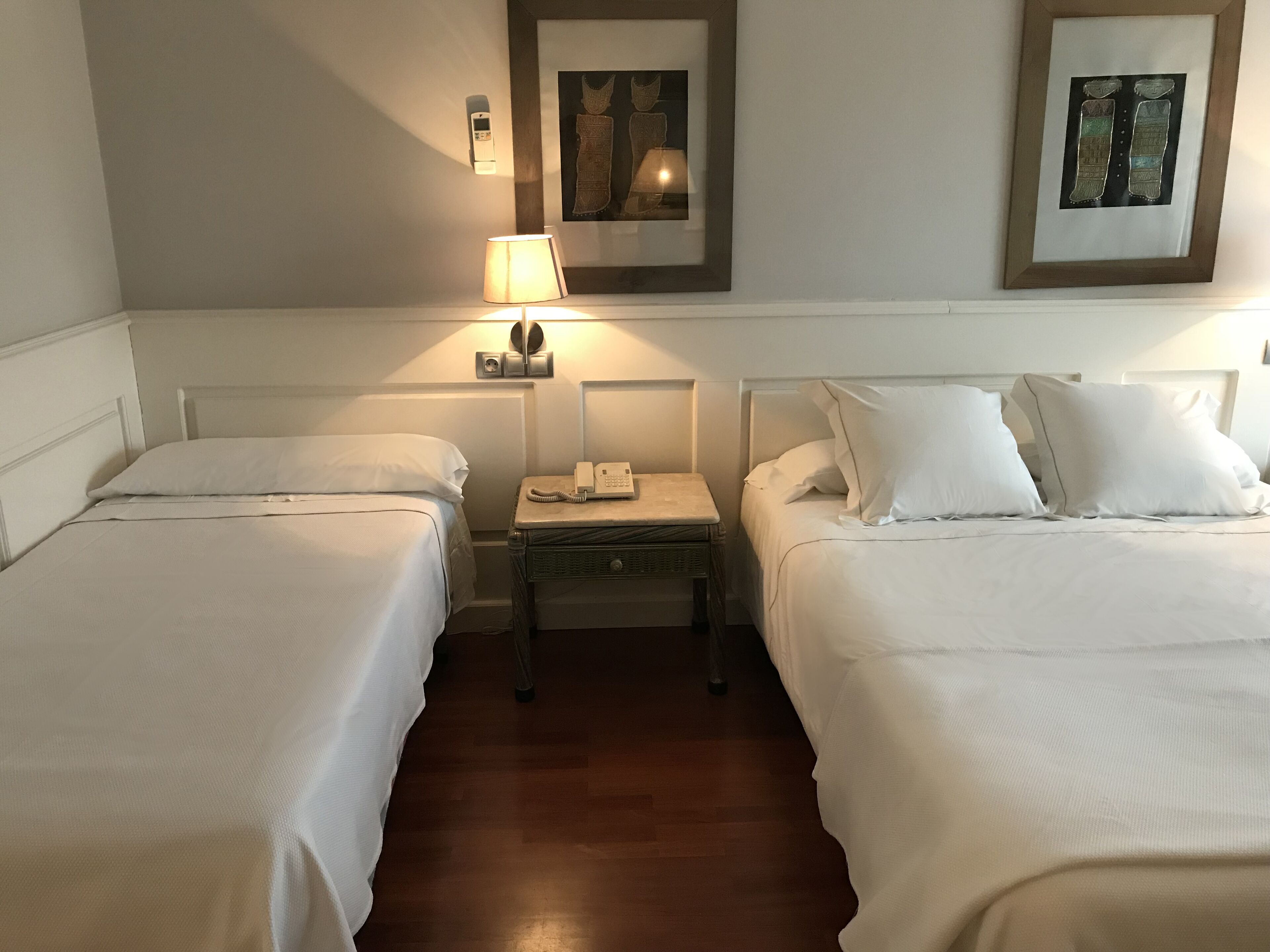 Une chambre d’hôtel avec deux lits simples, une table de chevet avec un téléphone et une lampe, et un tableau encadré au mur.