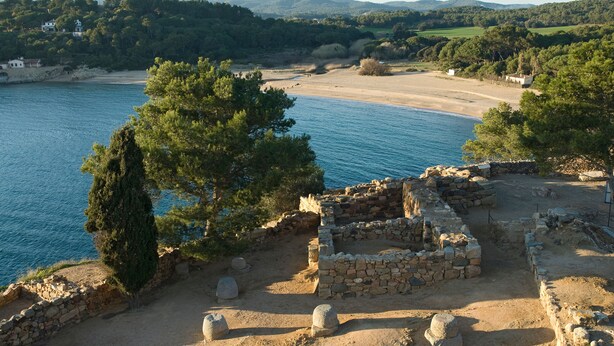 Un sitio arqueológico costero con ruinas de piedra y una playa.