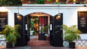 Entrada de un restaurante con fachada de azulejos, dos puertas negras y plantas en macetas.