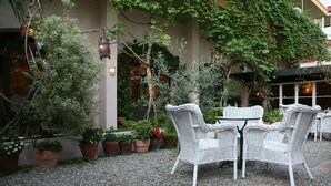 Un patio con mobiliario de mimbre, plantas en macetas y un edificio al fondo.