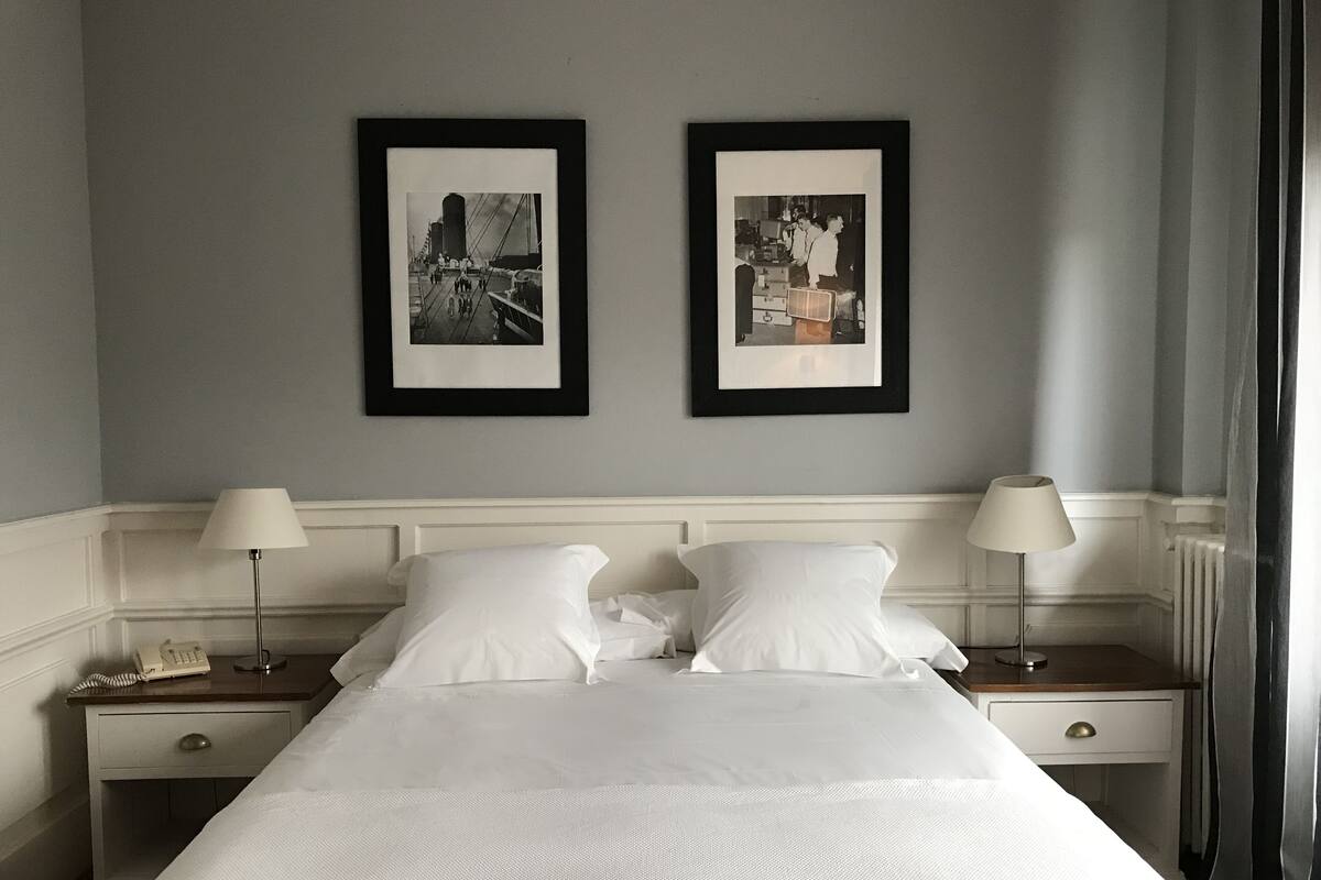 Ett hotellrum med en stor säng, två sängbord med lampor, en telefon och två inramade svartvita fotografier på väggen.