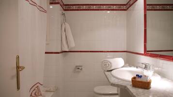 A bathroom with a white sink, a toilet, and a shower. There is a towel hanging on the wall and a basket with toiletries on the sink.
