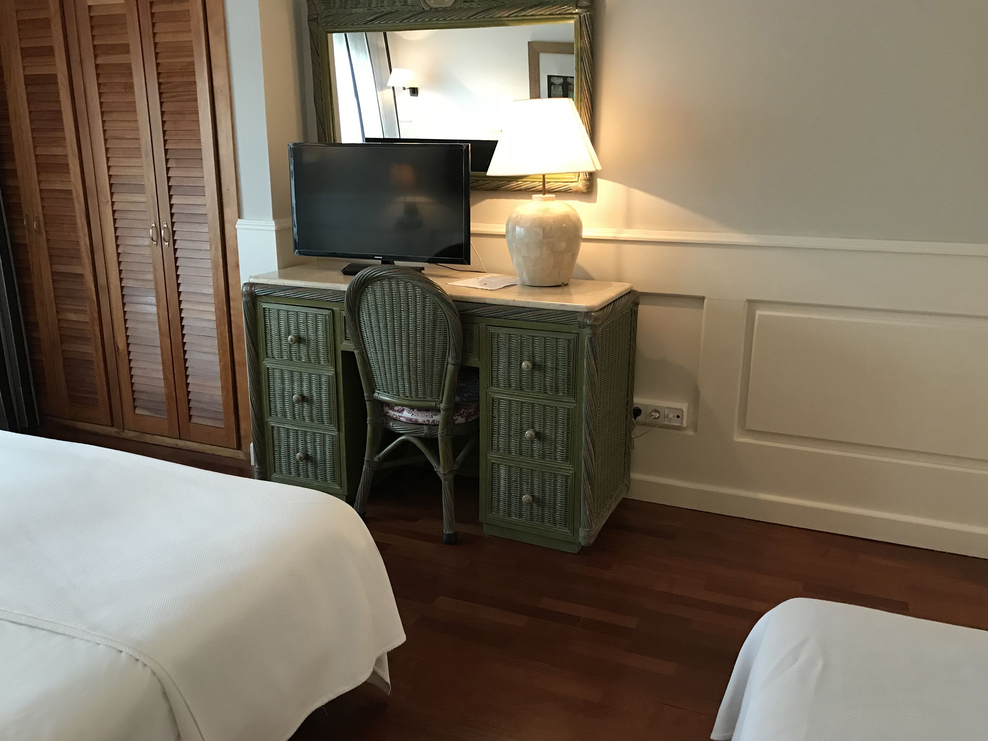Une chambre d’hôtel avec une armoire en bois, un bureau avec une télévision, une lampe et deux lits.