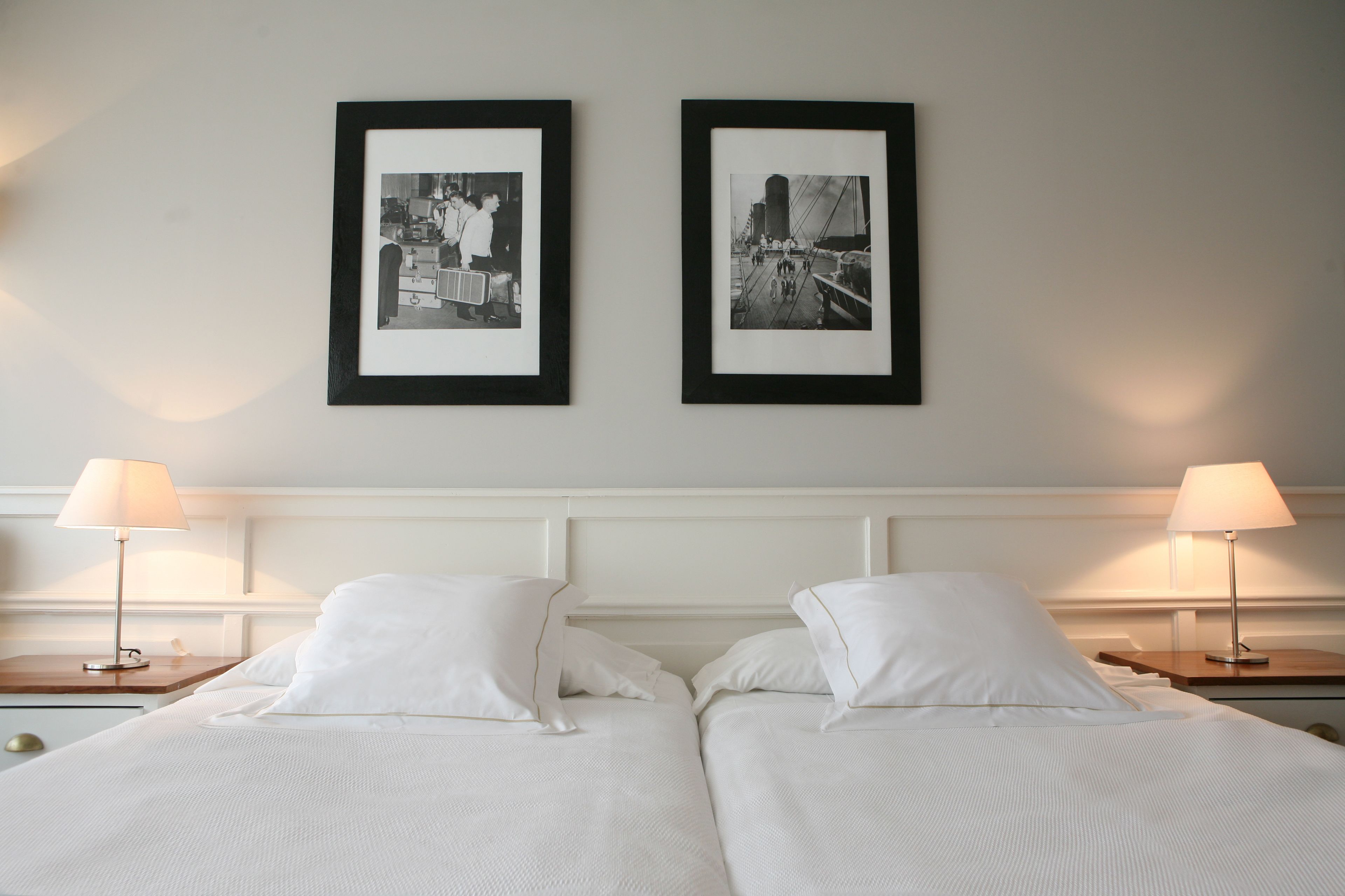 A hotel room with two beds, white bedding, and framed black-and-white photographs on the wall.