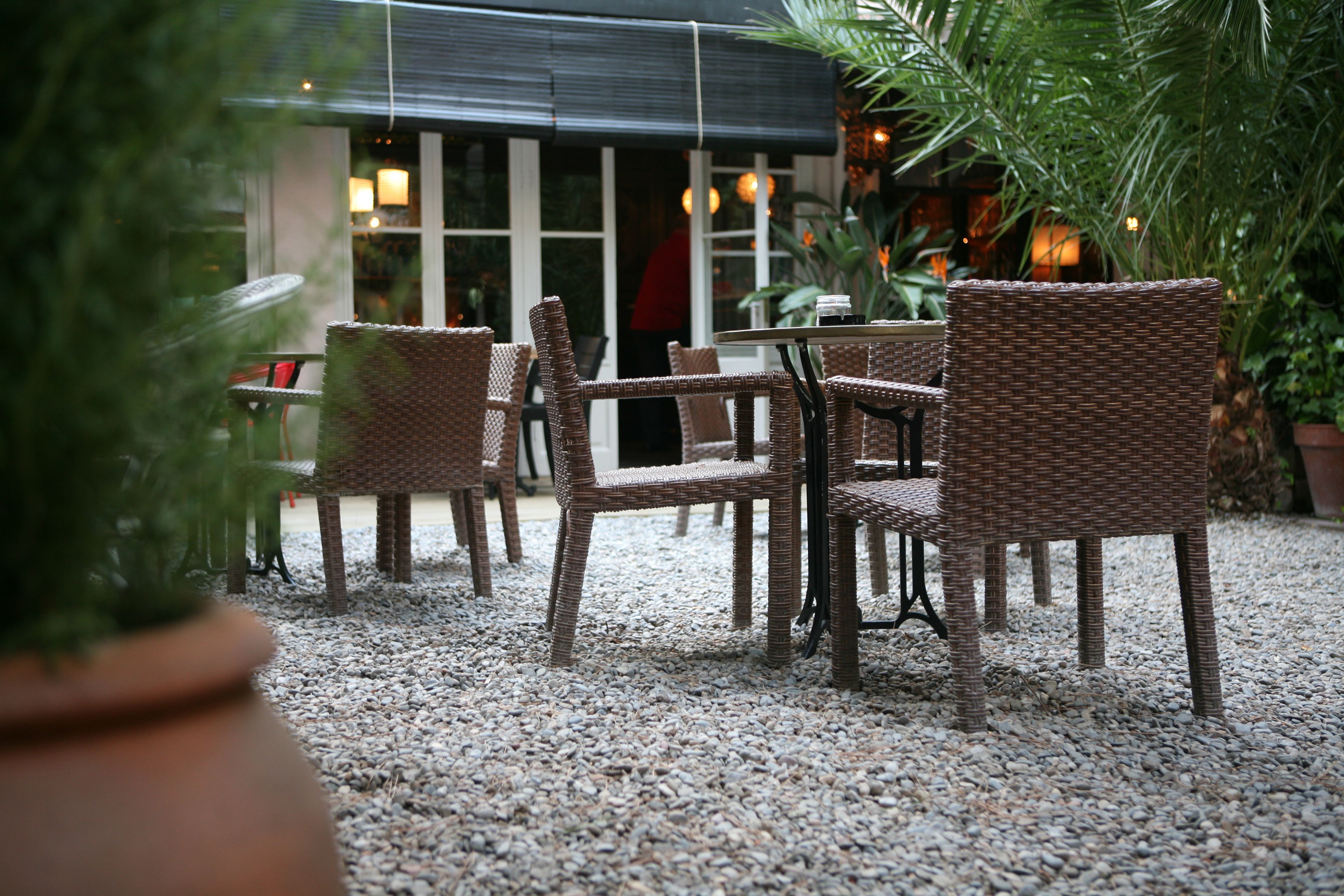 Wicker furniture, a gravel floor, and a building with windows and lights in the background.