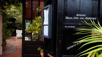 Uma porta de madeira preta com texto indicando um menu de Arrossos, oferecendo batatas fritas com batata palha e uma bebida.