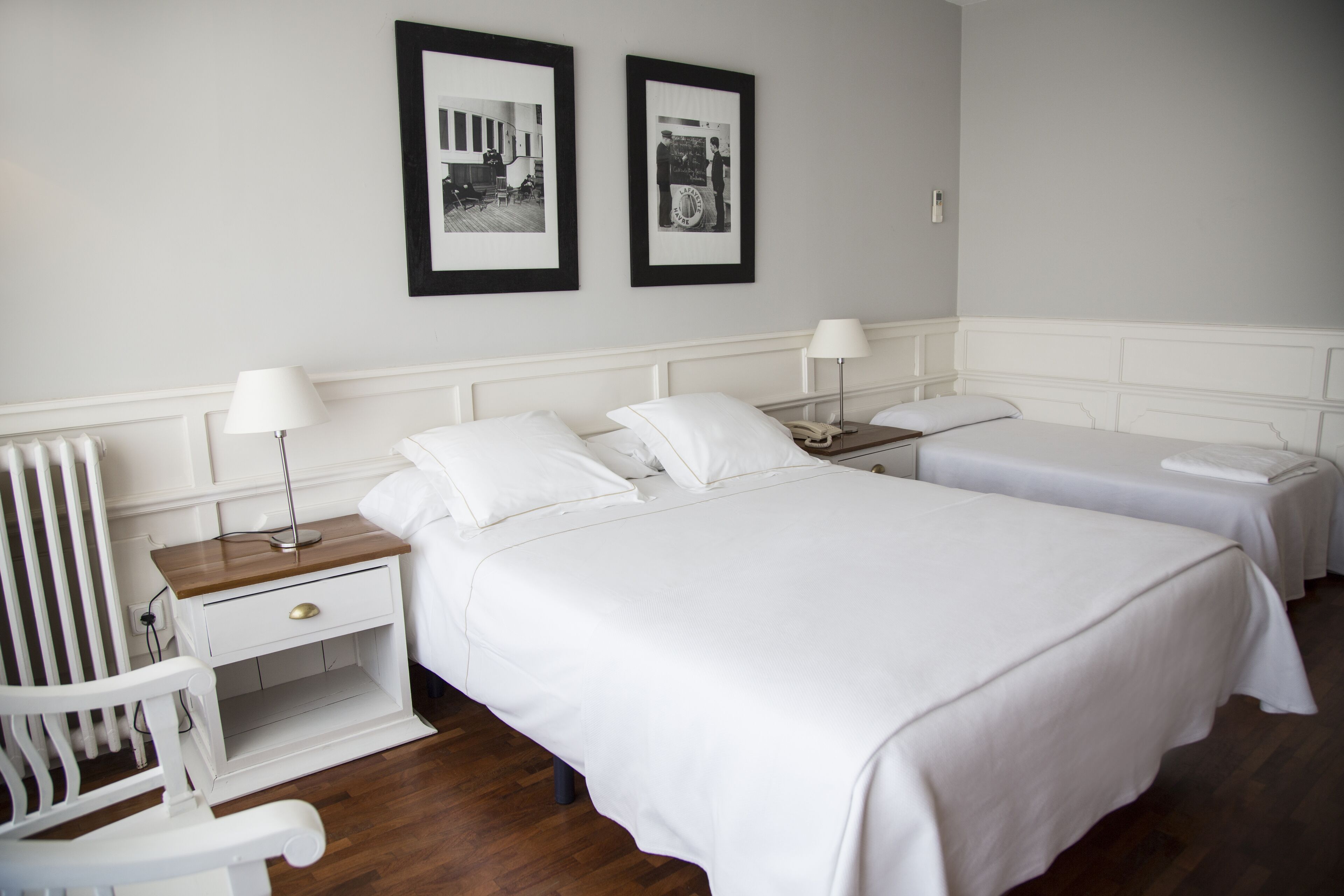 Une chambre d’hôtel avec deux lits simples, une table de chevet avec une lampe, une chaise et un tableau encadré au mur.