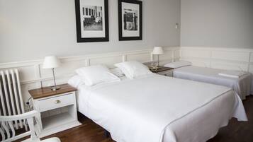 Habitación de hotel con dos camas individuales, una mesita de noche con lámpara, una silla y un cuadro en la pared.