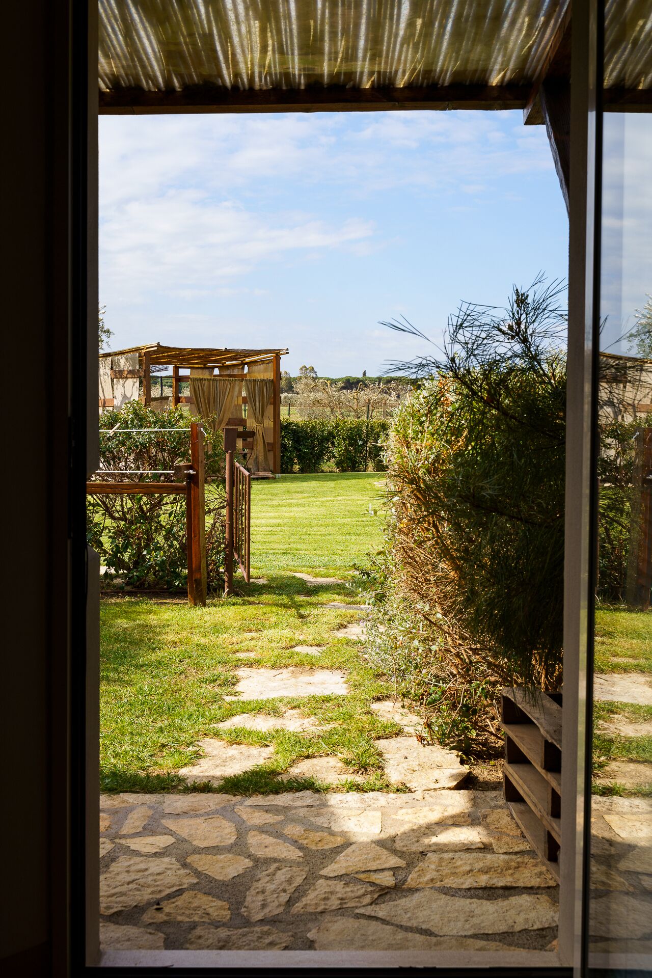 A stone pathway leading to a wooden pergola in a well-maintained garden with a clear sky.