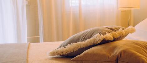 A bed with two pillows, a lamp, and sheer curtains in the background.