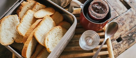 A tray of sliced bread, a jar of jam, and a spoon on a wooden table.