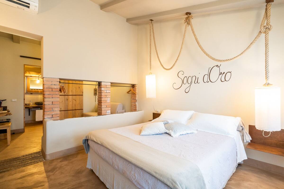 A hotel room with a large bed, a brick fireplace, and a wall-mounted sign reading "Sogni d'Oro".