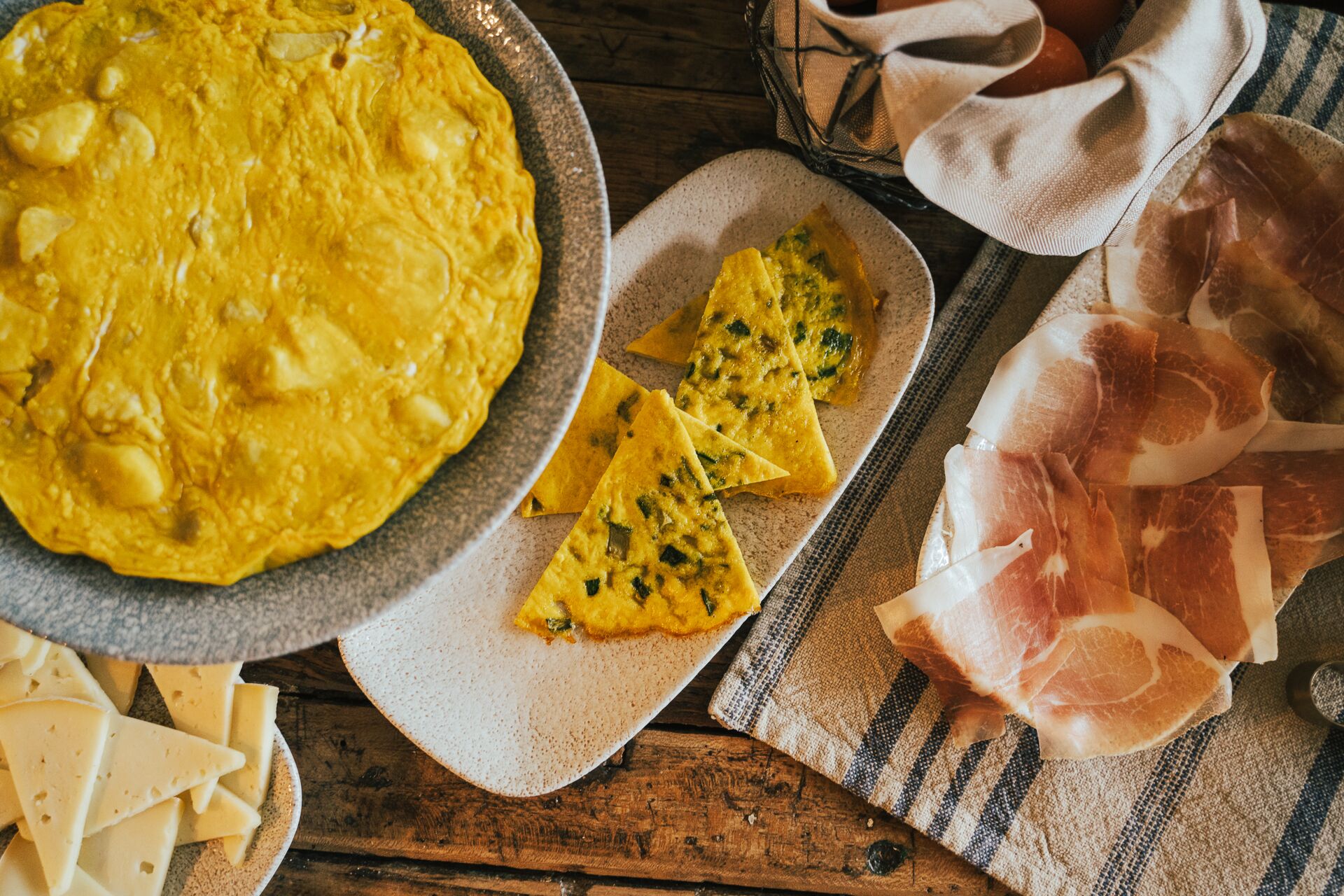 A plate of scrambled eggs, a slice of cheese, and a piece of prosciutto on a rustic wooden table.