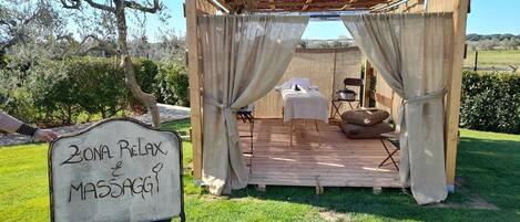 A massage area with a canopy, a massage table, a massage chair, and a sign reading "Zona Relax e Massaggio".