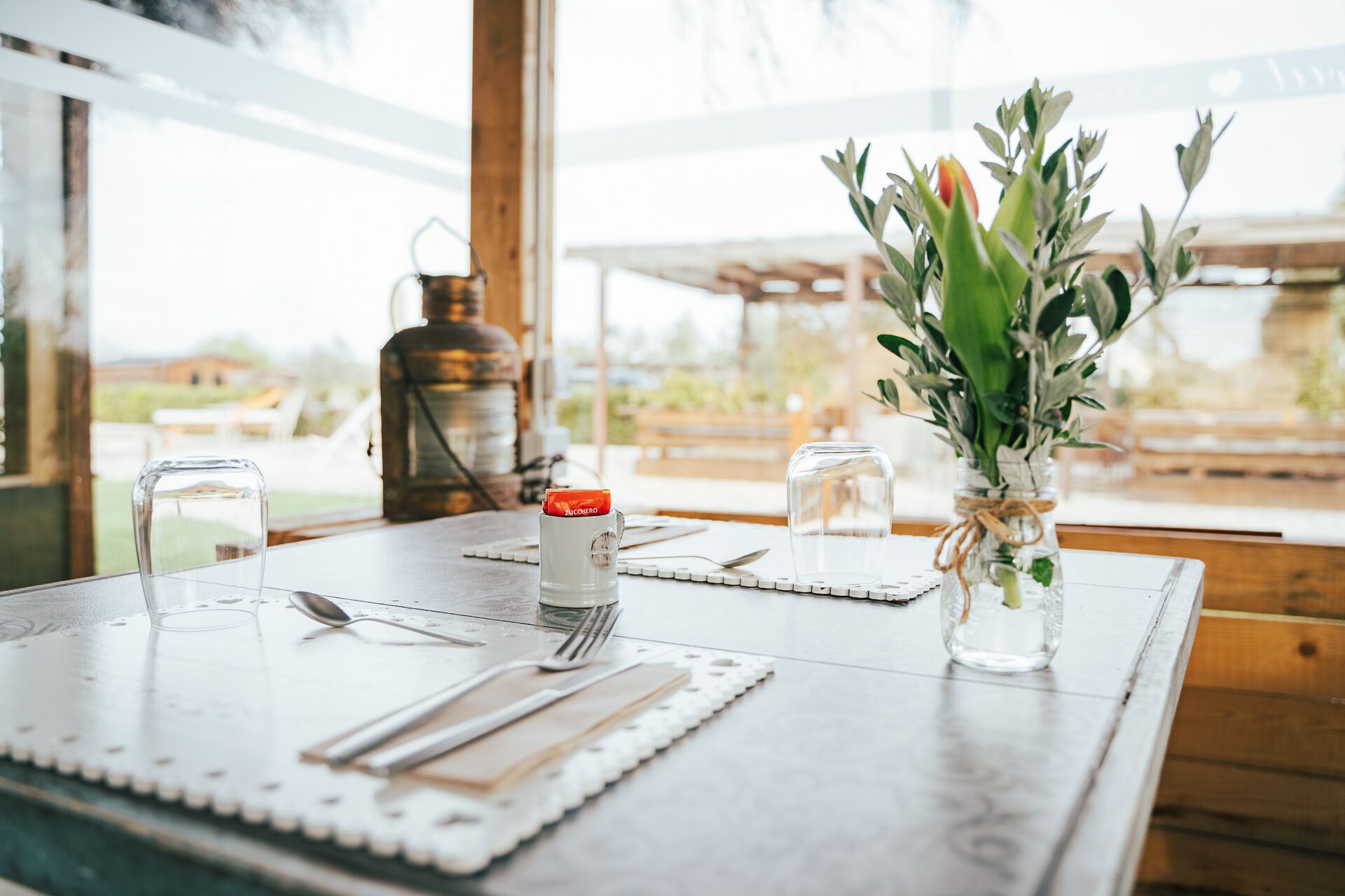 A dining table set with cutlery, a glass, a bottle, and a vase with flowers.