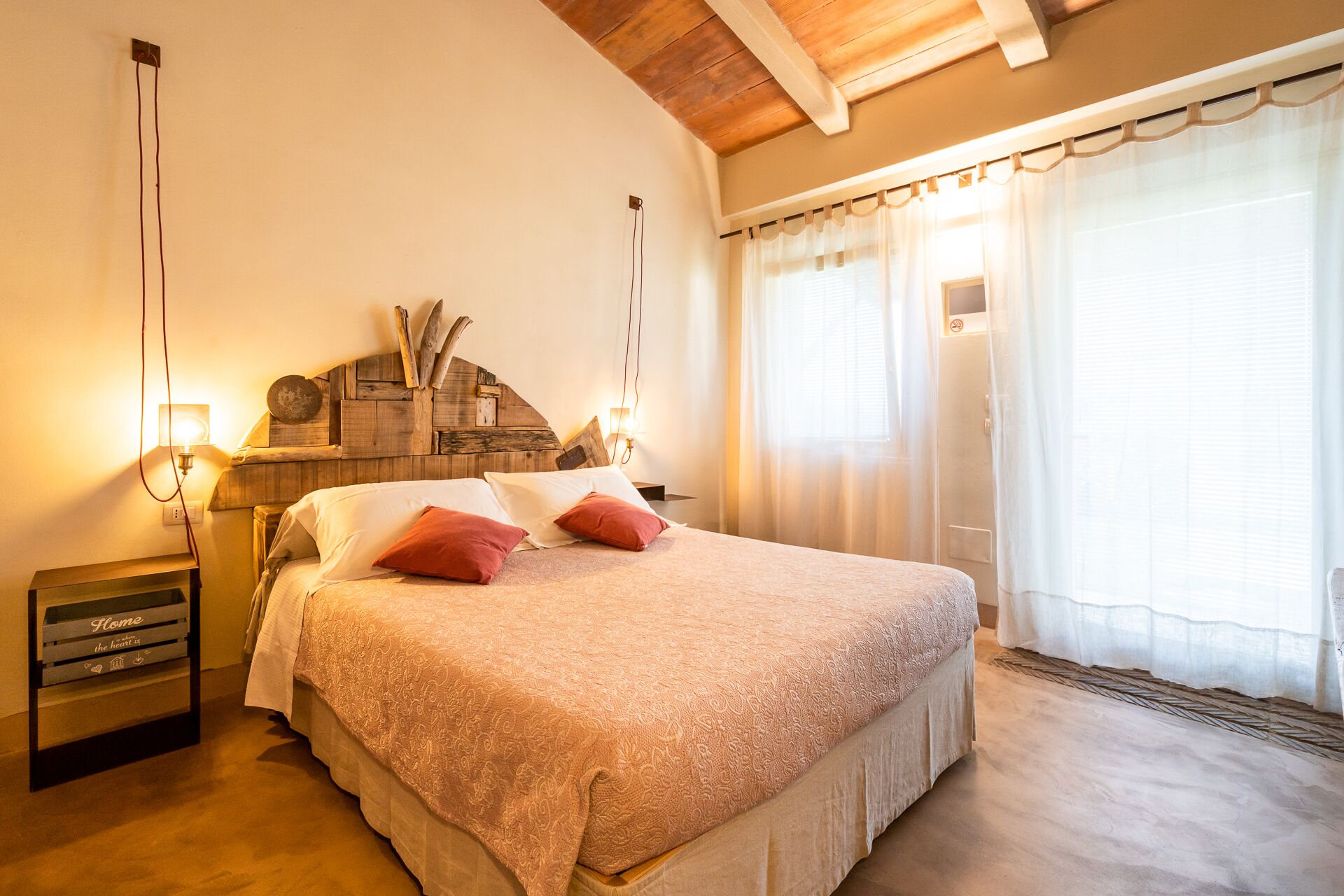 A bedroom with a large bed, wooden headboard, bedside lamps, and a window with sheer curtains.