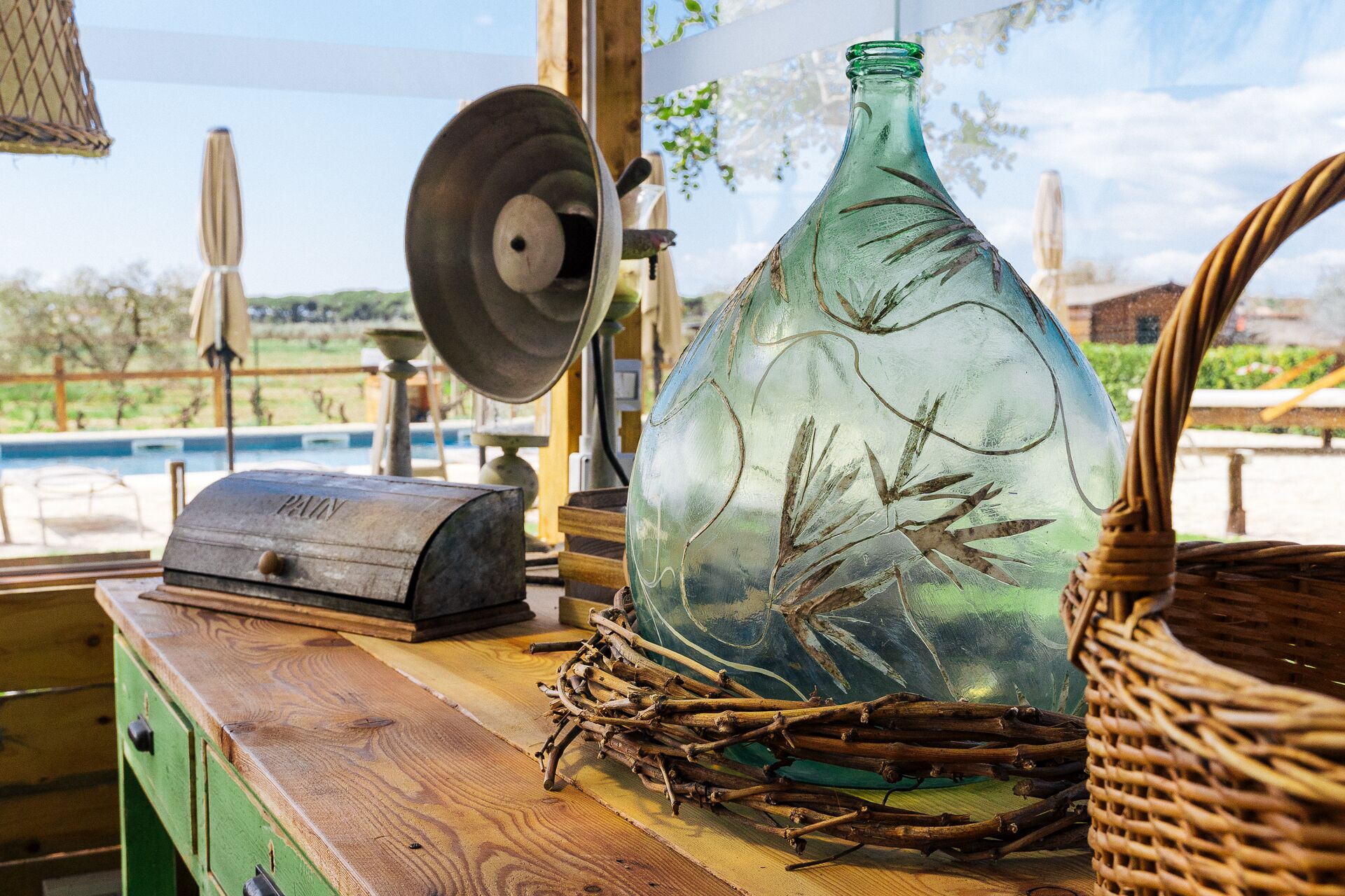 A rustic wooden table with a green metal object, a woven basket, and a metal tool.