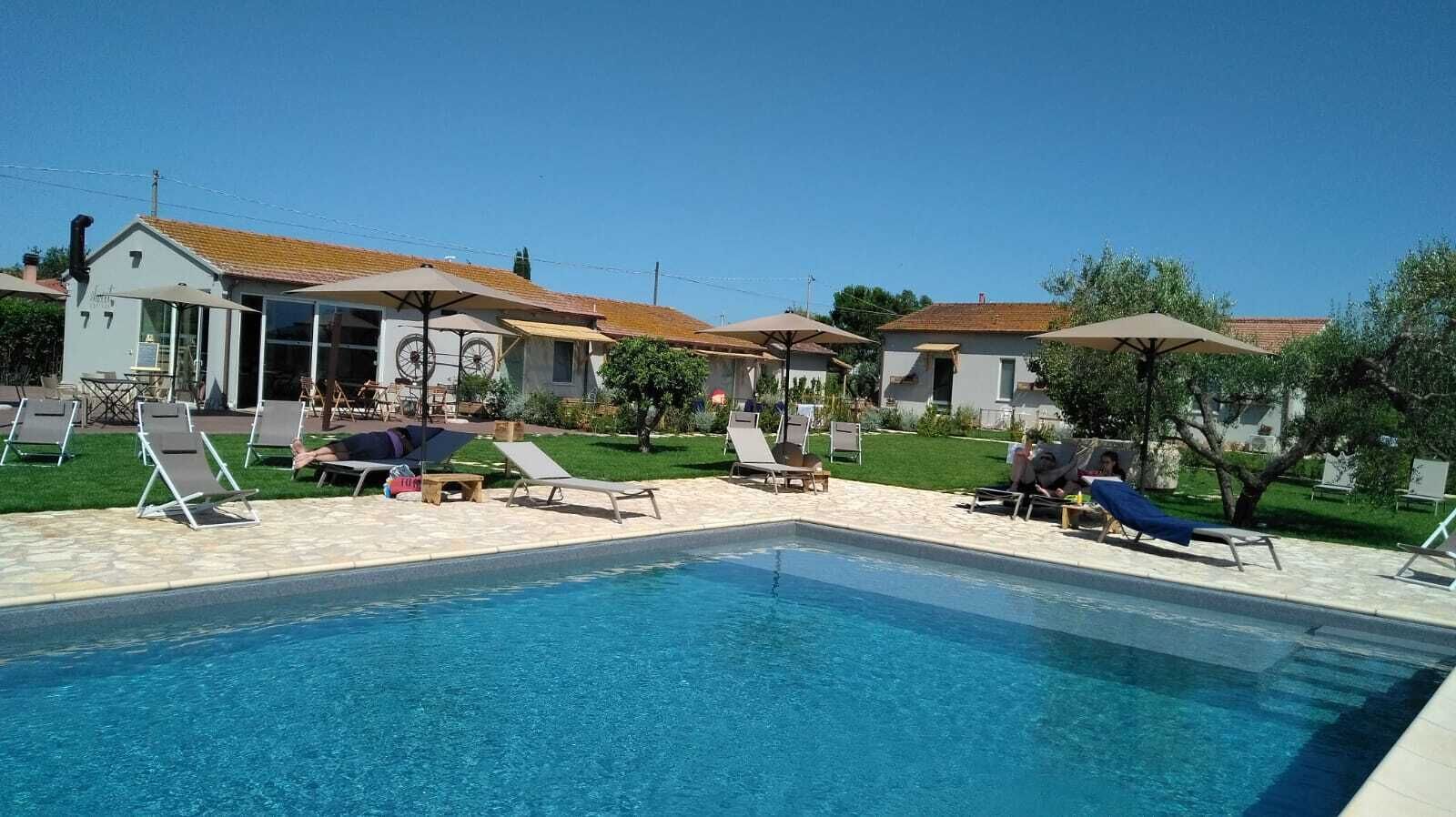 A swimming pool with lounge chairs and umbrellas, surrounded by buildings with tiled roofs and a clear sky.