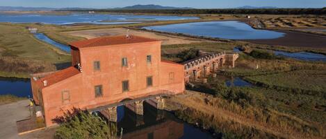 Un ampio edificio a un solo piano con tetto in tegole rosse, situato vicino a uno specchio d'acqua con diverse vasche più piccole e un ponte che collega un'altra costruzione.
