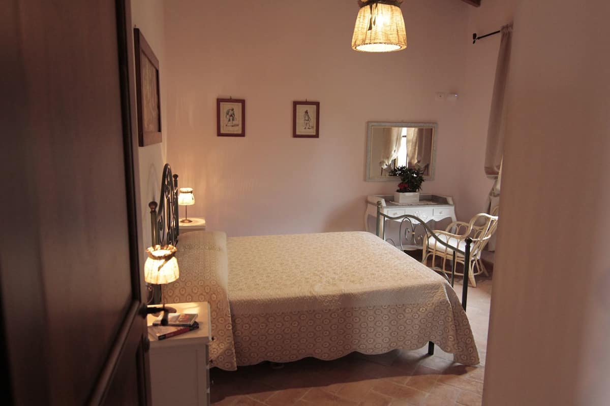 Un dormitorio con cama, mesita de noche, lámpara, silla y cómoda.