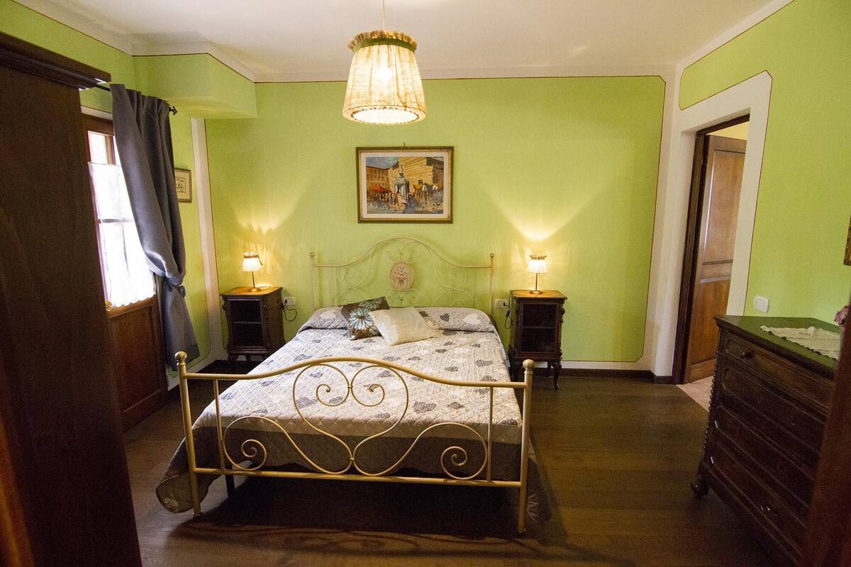 Un dormitorio con estructura metálica para la cama, dos mesitas de noche con lámparas, un aparador de madera y un cuadro en la pared.