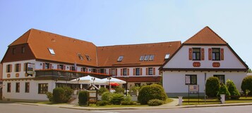 Um hotel com arquitetura europeia tradicional, apresentando um amplo pátio com área de estar externa e um jardim bem cuidado.