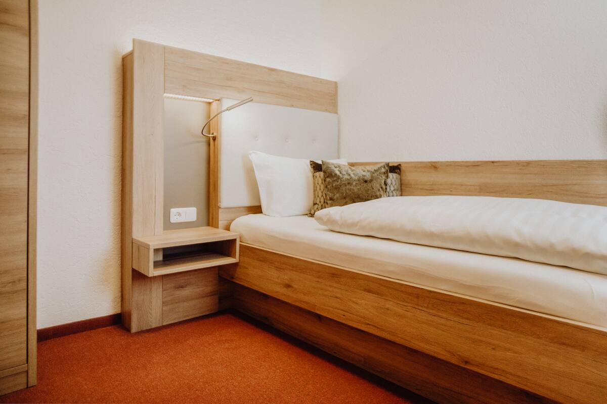 A bedroom with a wooden bed, a nightstand, a mirror, and a wall socket.