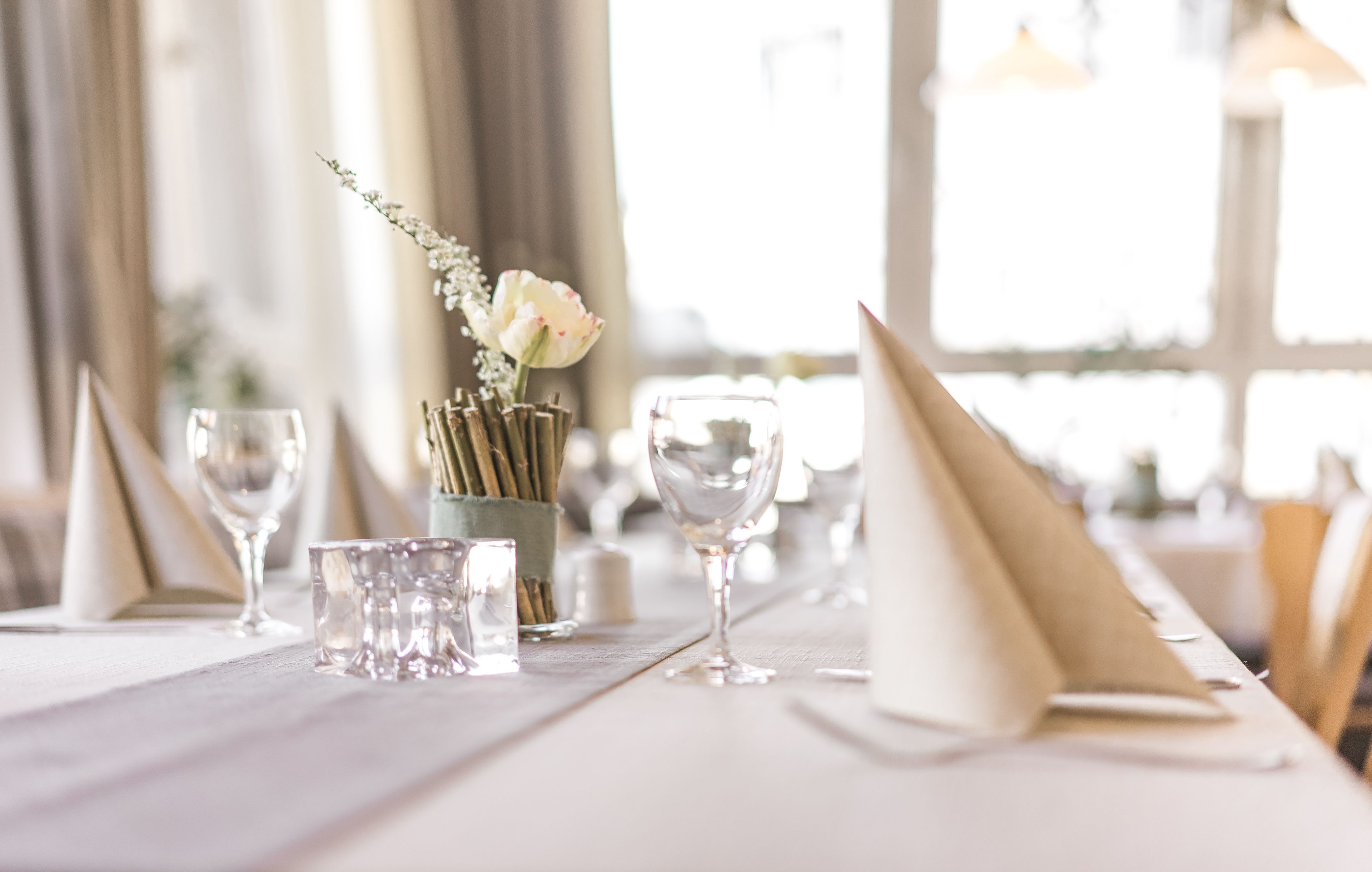 Una mesa de comedor dispuesta con cristalería transparente, un florero con flores y una vela.