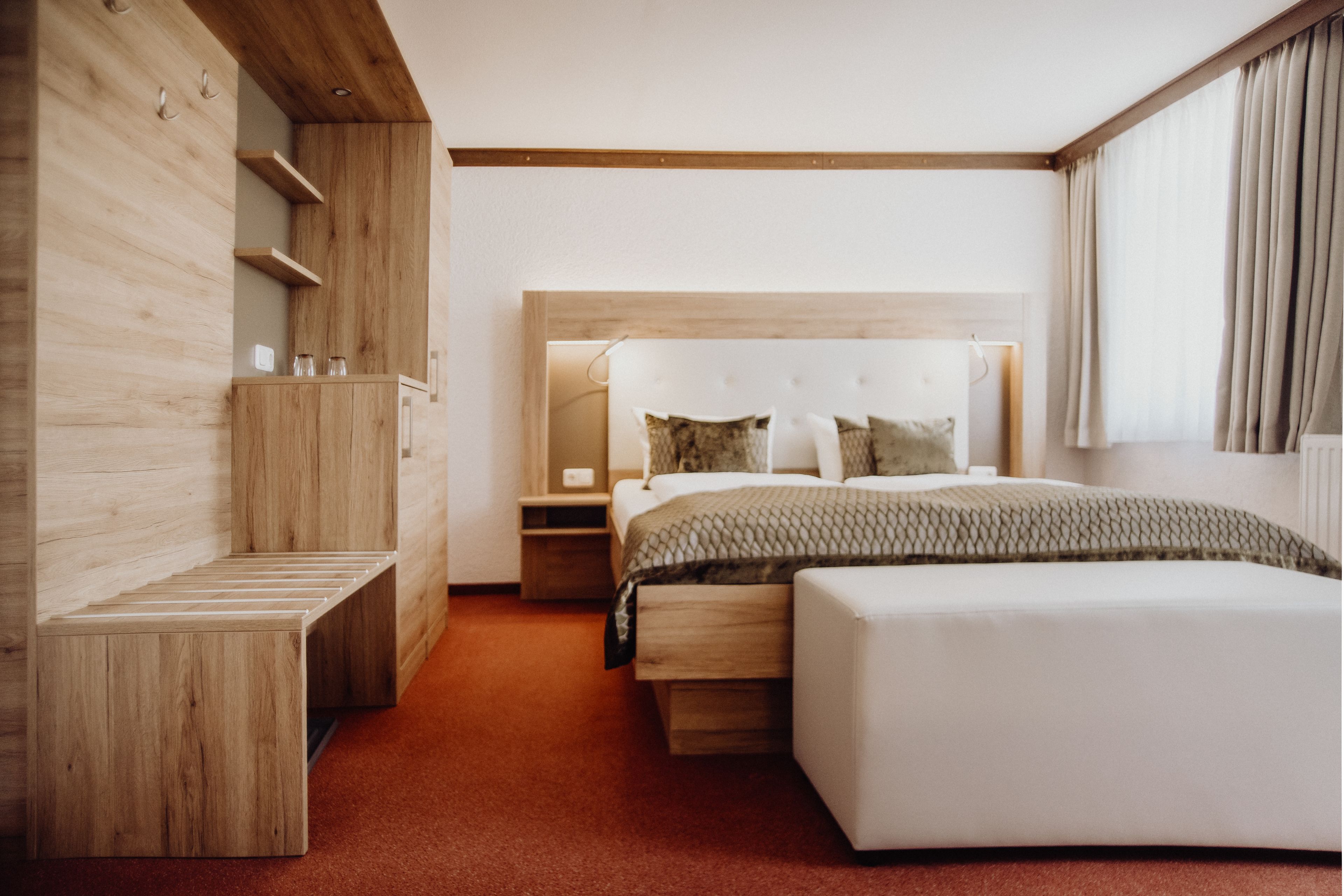 A modern bedroom with a wooden wardrobe, a bed with a headboard, and a window with curtains.