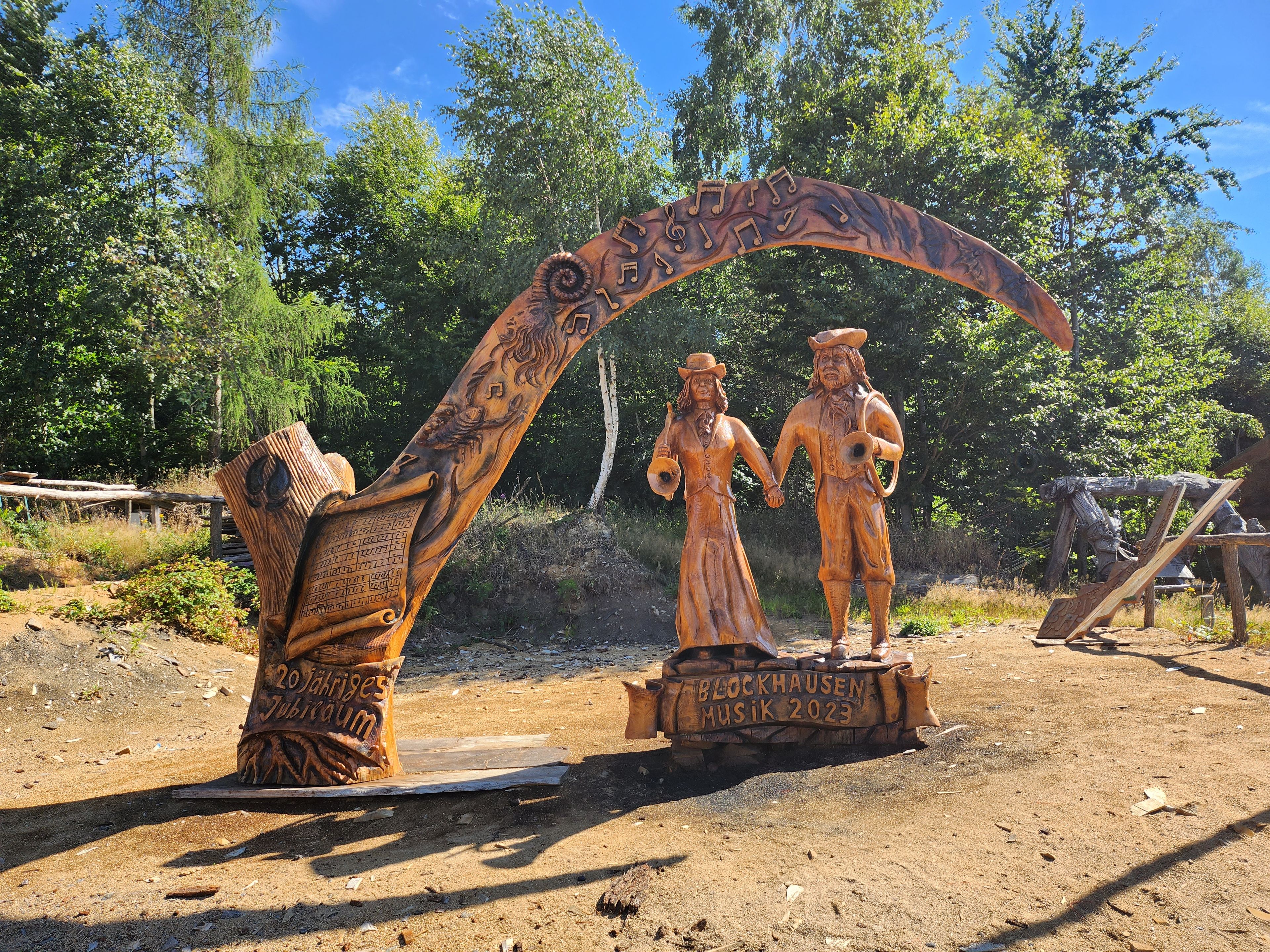 Eine rustikale, freistehende Skulptur zeigt ein Mann und eine Frau, die Händchen halten, umgeben von Bäumen.