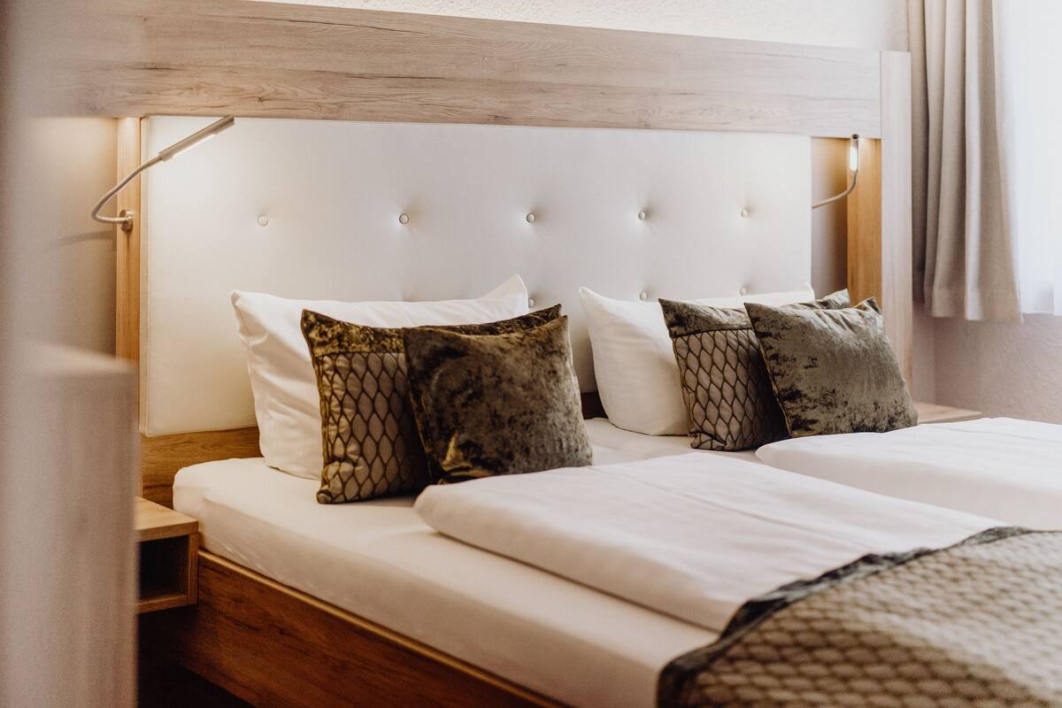 A neatly made bed with white linens and patterned pillows, a wooden headboard, and a bedside table with a lamp.