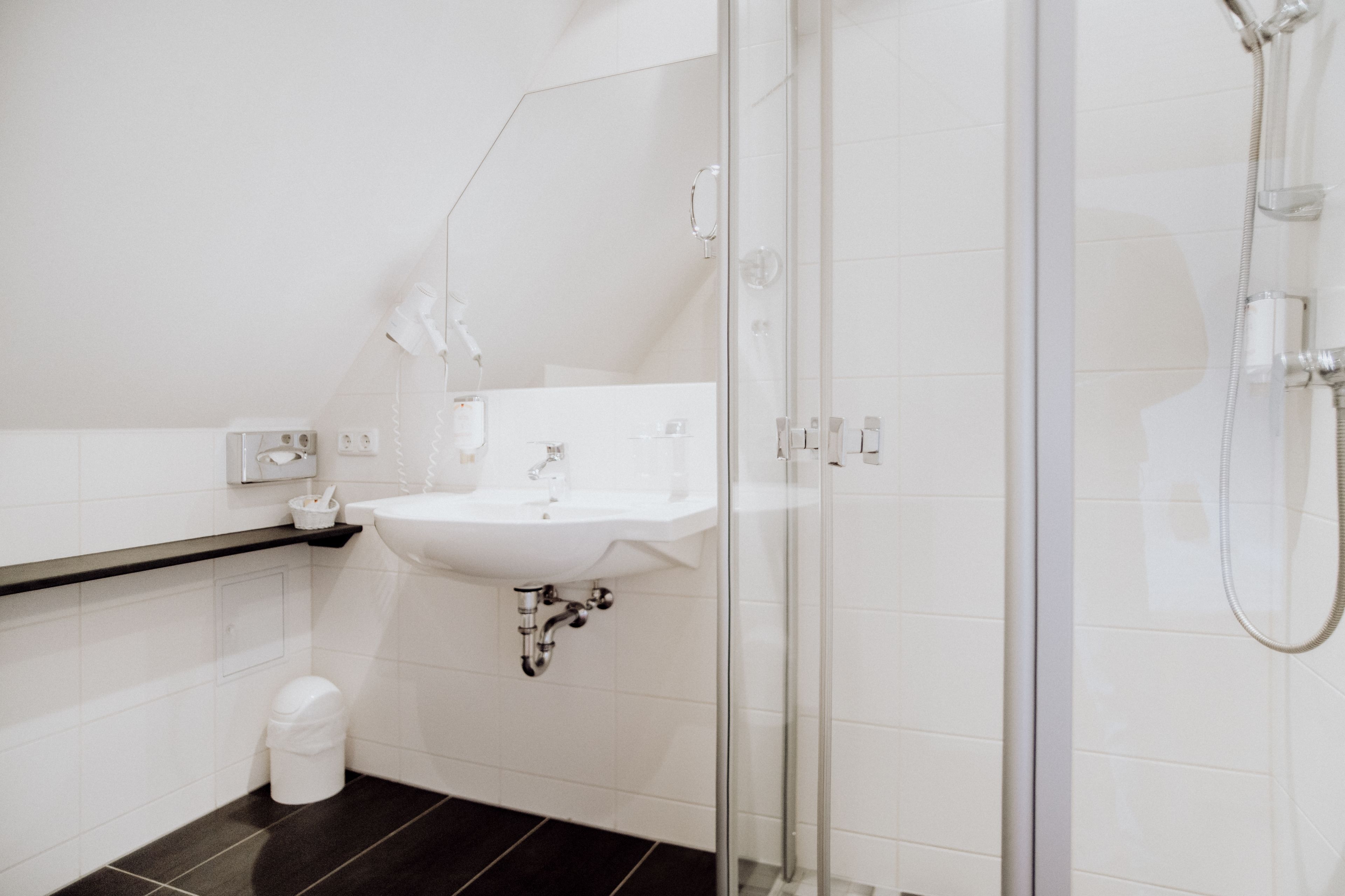 A modern bathroom with a glass shower enclosure, a white sink, and a black tiled floor.
